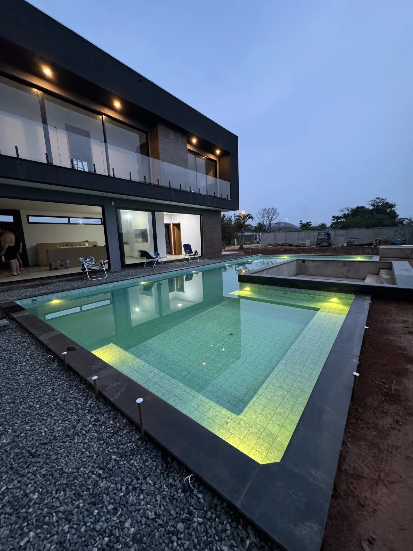 Piscina iluminada ao entardecer em frente à casa