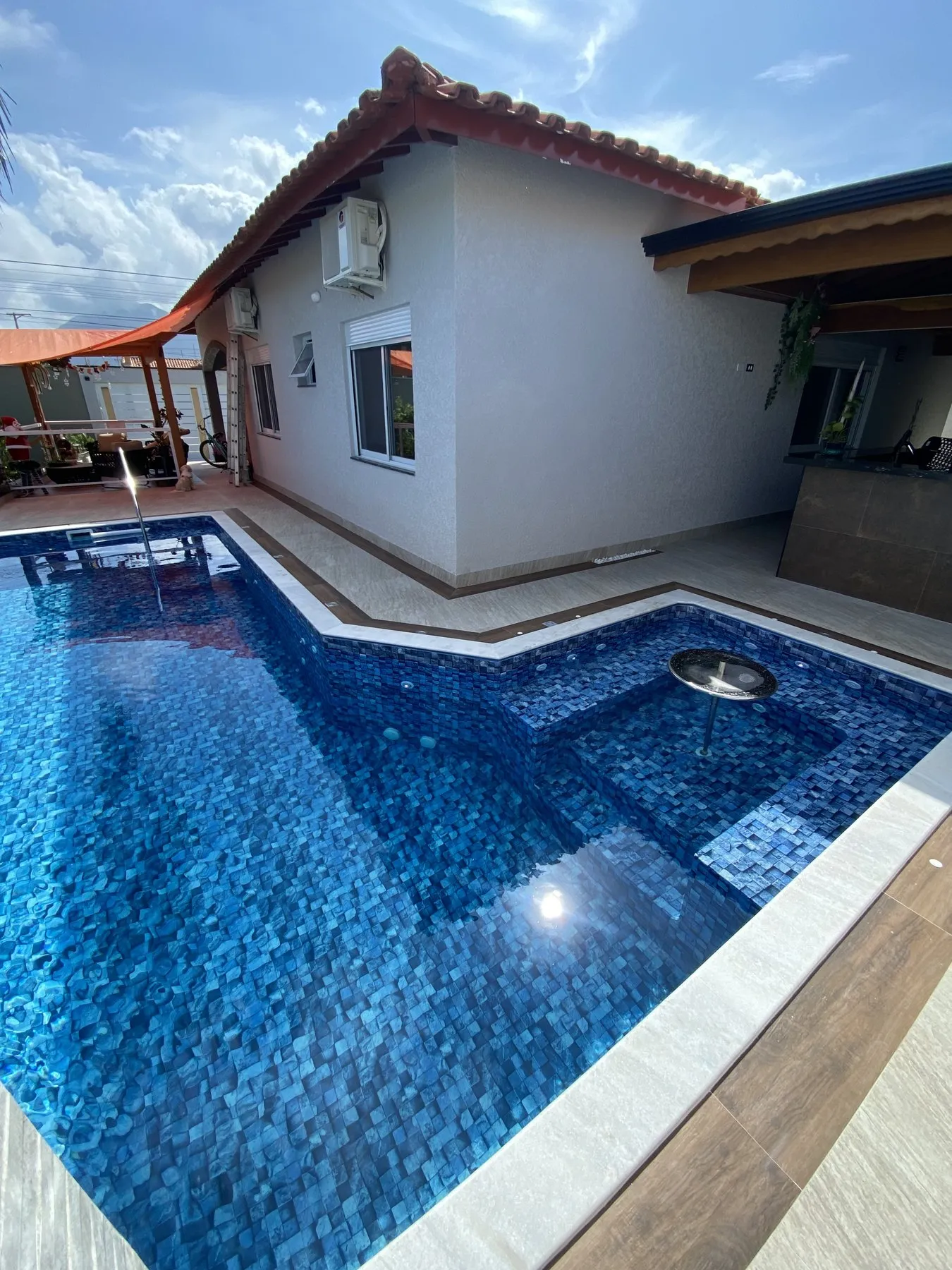 Piscina em L ao lado da casa com pastilhas azuis